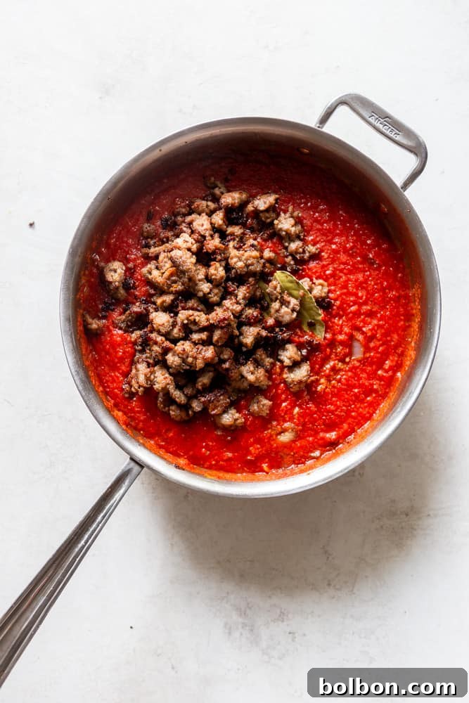 Hearty One-Pan Gnocchi & Sausage 5 A skillet filled with a vibrant tomato marinara sauce, with browned ground sausage mixed in and a bay leaf gently simmering, creating a rich base for the gnocchi.