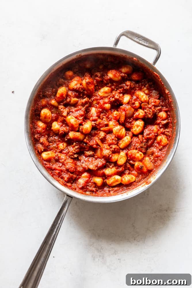 Hearty One-Pan Gnocchi & Sausage 6 One-Pot Gnocchi with Sausage simmering in a skillet, before the addition of ricotta and mozzarella cheese, showing the gnocchi fully immersed in the rich tomato sauce.