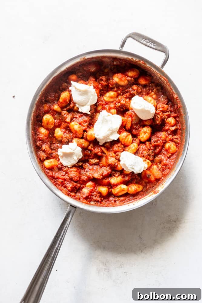 Hearty One-Pan Gnocchi & Sausage 7 One-Pot Gnocchi with Sausage in a skillet, generously dolloped with creamy ricotta cheese, ready for the mozzarella and final melting.