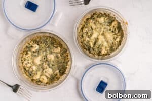 Effortless Weekly Chicken Bake 8 Two round glass containers filled with a cheesy, baked spinach and chicken casserole, with matching plastic lids nearby and two metal forks on a white marble surface.