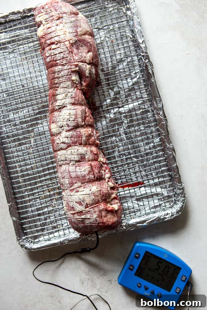 Uncooked beef tenderloin, tied with kitchen twine and generously rubbed with softened butter, ready for slow roasting.