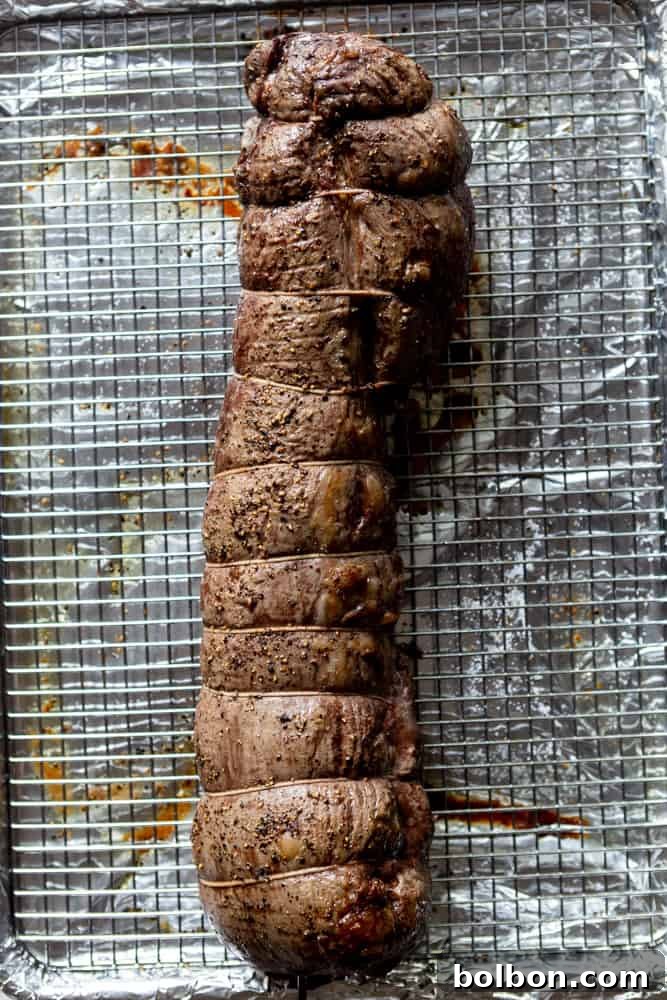 A perfectly slow-roasted beef tenderloin, golden brown and resting on a rack over a sheet pan, before the final sear.