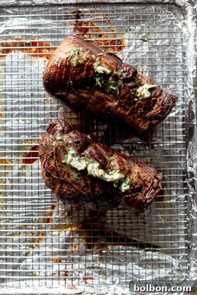 A perfectly cooked beef tenderloin, sliced in half, revealing a rosy medium-rare center, topped with a generous dollop of aromatic herb butter.