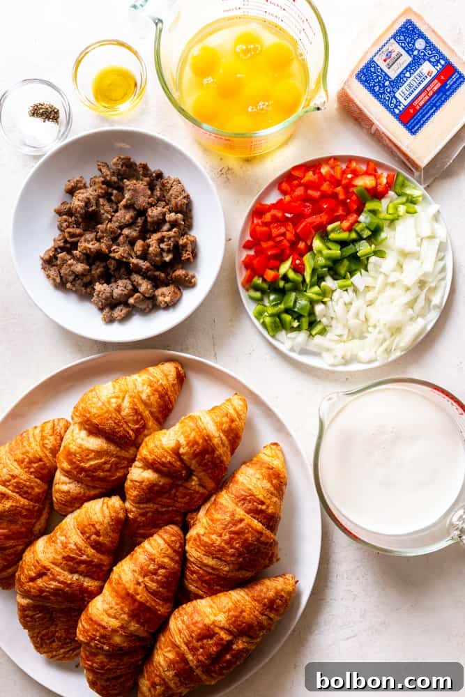 Key ingredients for the Overnight Croissant Breakfast Casserole laid out: croissants, milk and cream, breakfast sausage, colorful bell peppers, onions, eggs, and a block of Gruyere cheese, along with salt, pepper, and olive oil.