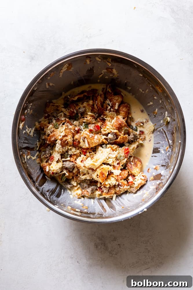 The fully mixed Overnight Croissant Breakfast Casserole ingredients in a bowl, showing the combination of croissants, sausage, vegetables, and cheese coated in custard.