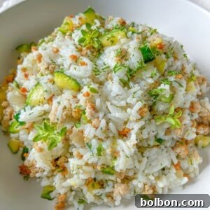 A white bowl filled with Zucchini Rice—cooked white rice mixed with chopped zucchini, ground meat, grated carrots, and topped with fresh green herbs—makes for a perfect meal prep easy meal.