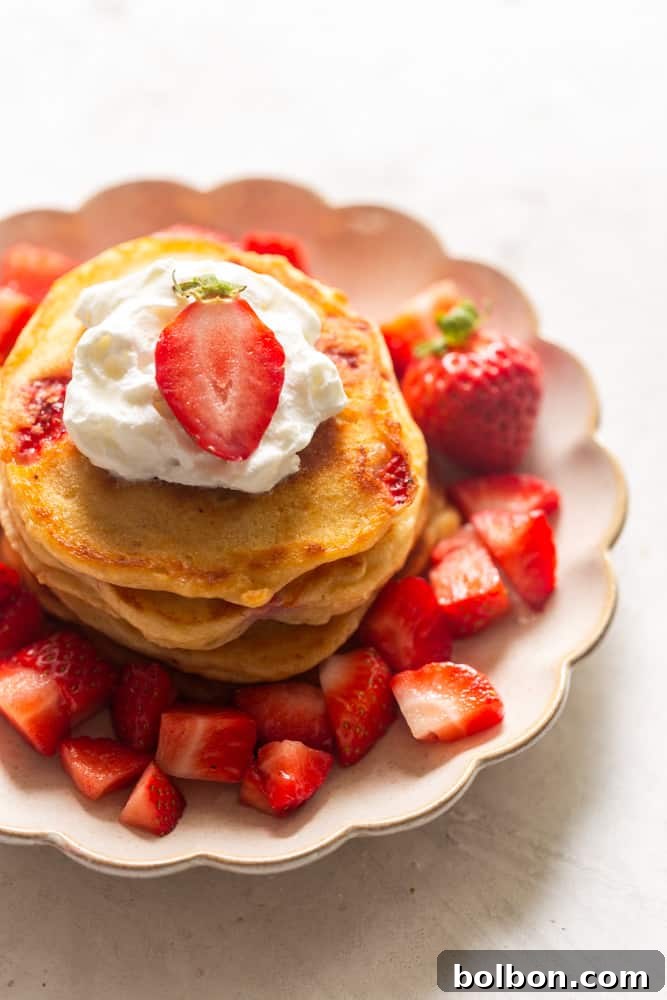A stack of strawberry pancakes topped with whipped cream and a fresh strawberry.