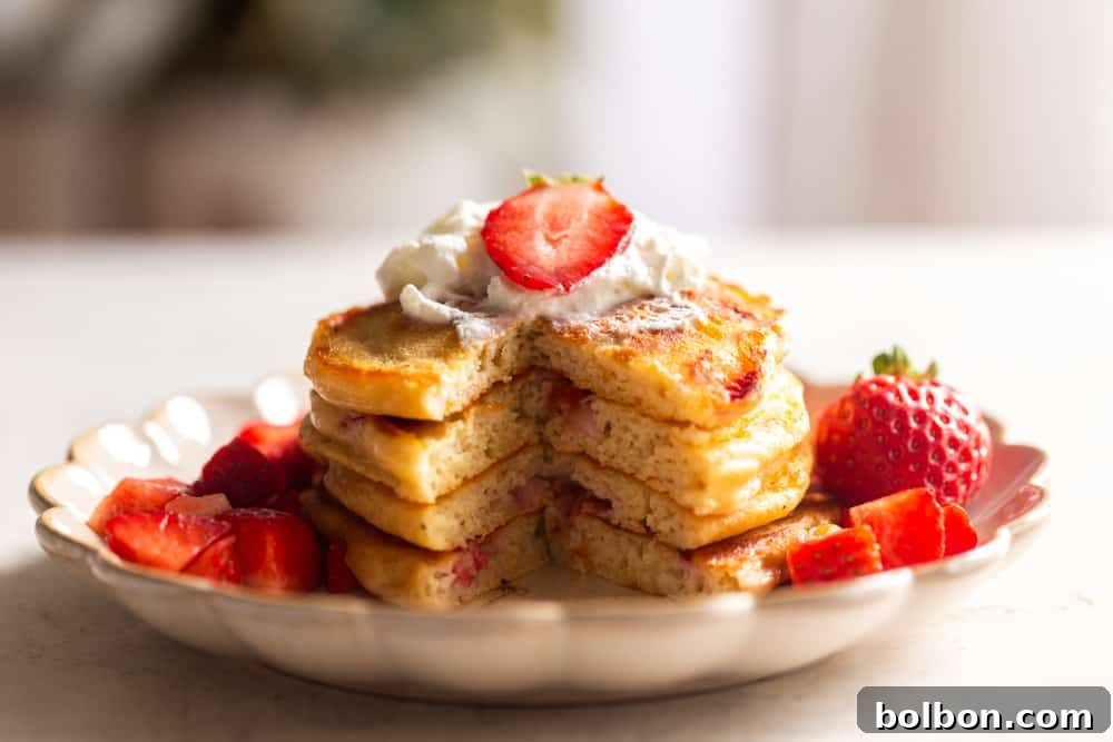 Strawberry pancakes after being cut, topped with whipped cream and strawberries.