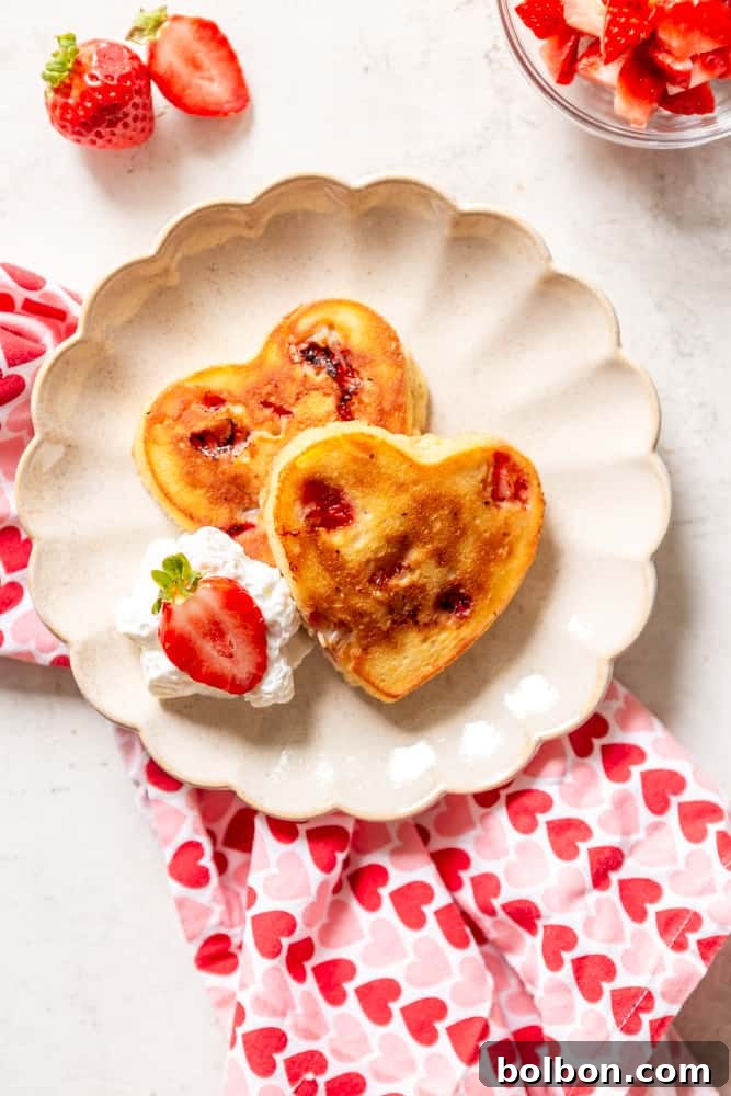 heart shaped strawberry pancakes on a scalloped plate with a heart napkin.