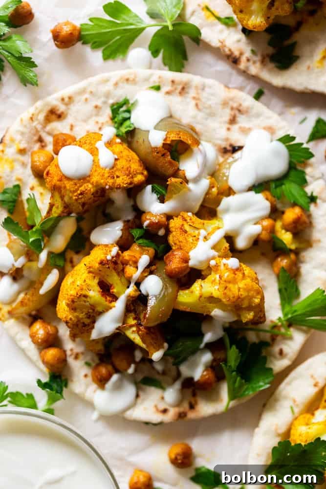 Roasted spiced Cauliflower and chickpeas on a pita, drizzled with garlic yogurt sauce and garnished with fresh parsley. A complete and inviting vegetarian meal.