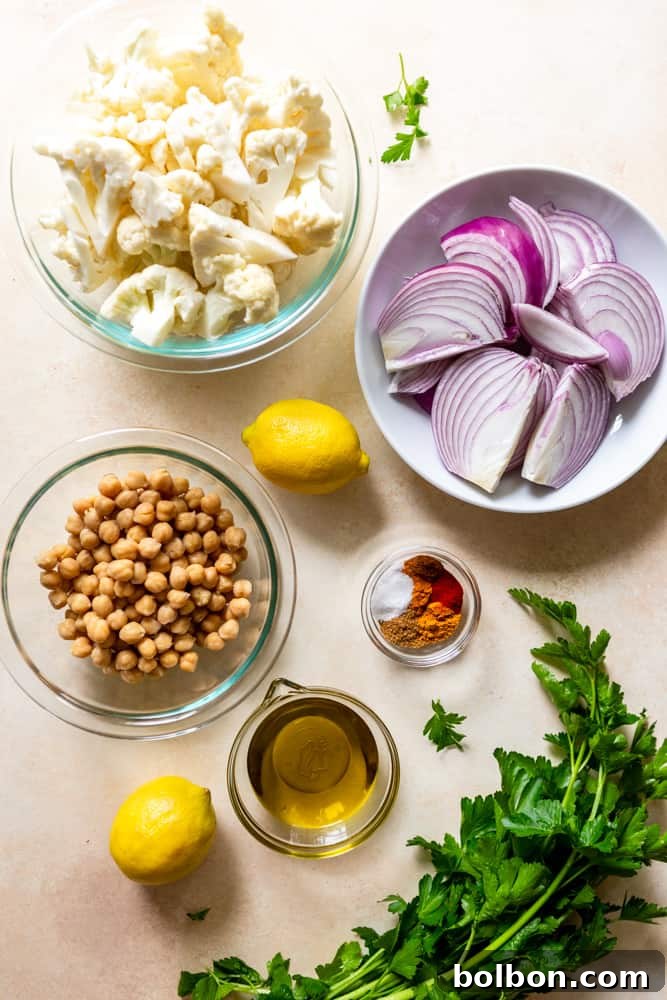 Fresh ingredients for Cauliflower Chickpea Pitas laid out: vibrant cauliflower florets, sliced red onion, canned chickpeas, olive oil, a selection of colorful spices, salt, and fresh parsley sprigs.
