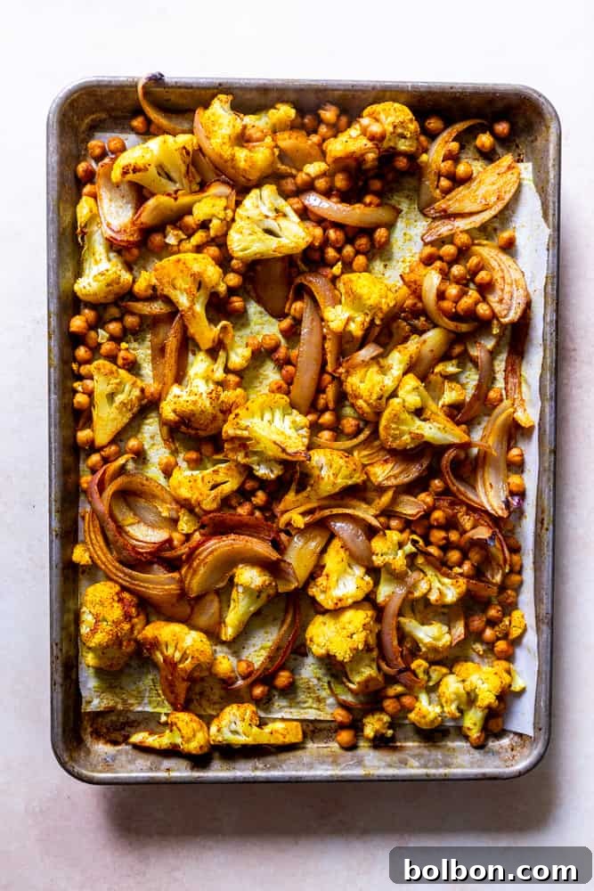 Sheet pan showcasing perfectly roasted spiced cauliflower, crispy chickpeas, and caramelized onions, golden brown and fragrant, fresh out of the oven.