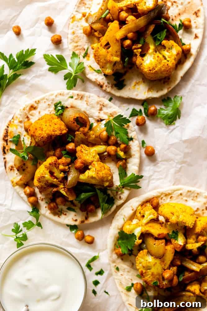Two open pitas filled with golden roasted spiced cauliflower and chickpeas, artfully arranged and garnished with vibrant green parsley, ready to be enjoyed.