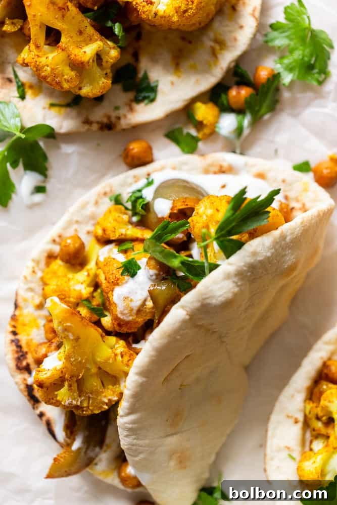 Close-up of a generously filled pita with spiced cauliflower and chickpeas, drizzled with creamy garlic yogurt sauce, and garnished with vibrant fresh parsley, ready to be eaten.