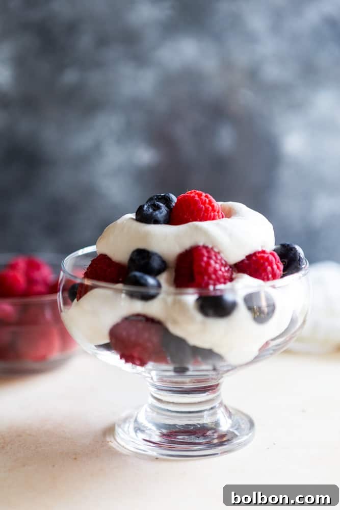 Homemade vanilla whipped cream generously dolloped on a dessert with fresh raspberries and blueberries in a clear glass bowl, ready to be enjoyed.