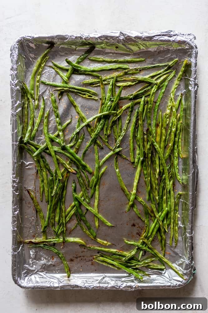 Perfectly roasted green beans spread out on a sheet pan, showcasing their tender-crisp texture and slightly browned edges. This image represents the final stage of cooking before serving.