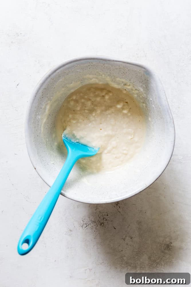 Buttermilk Waffle batter resting in a ceramic bowl with a blue spatula, showing its perfect consistency.