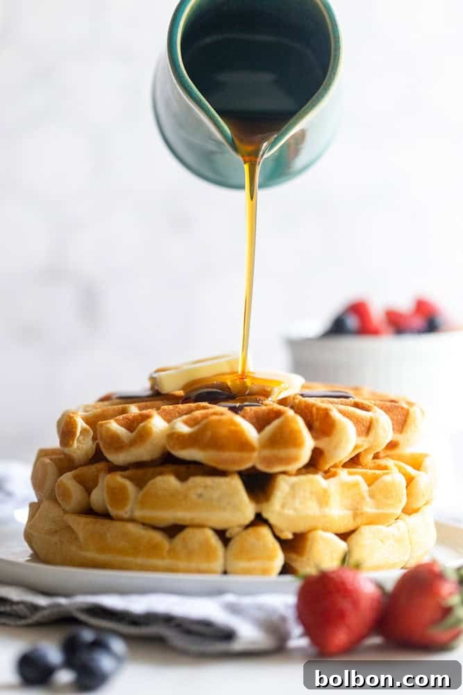 A stack of fluffy buttermilk waffles with golden maple syrup being poured over them, creating a mouth-watering cascade.