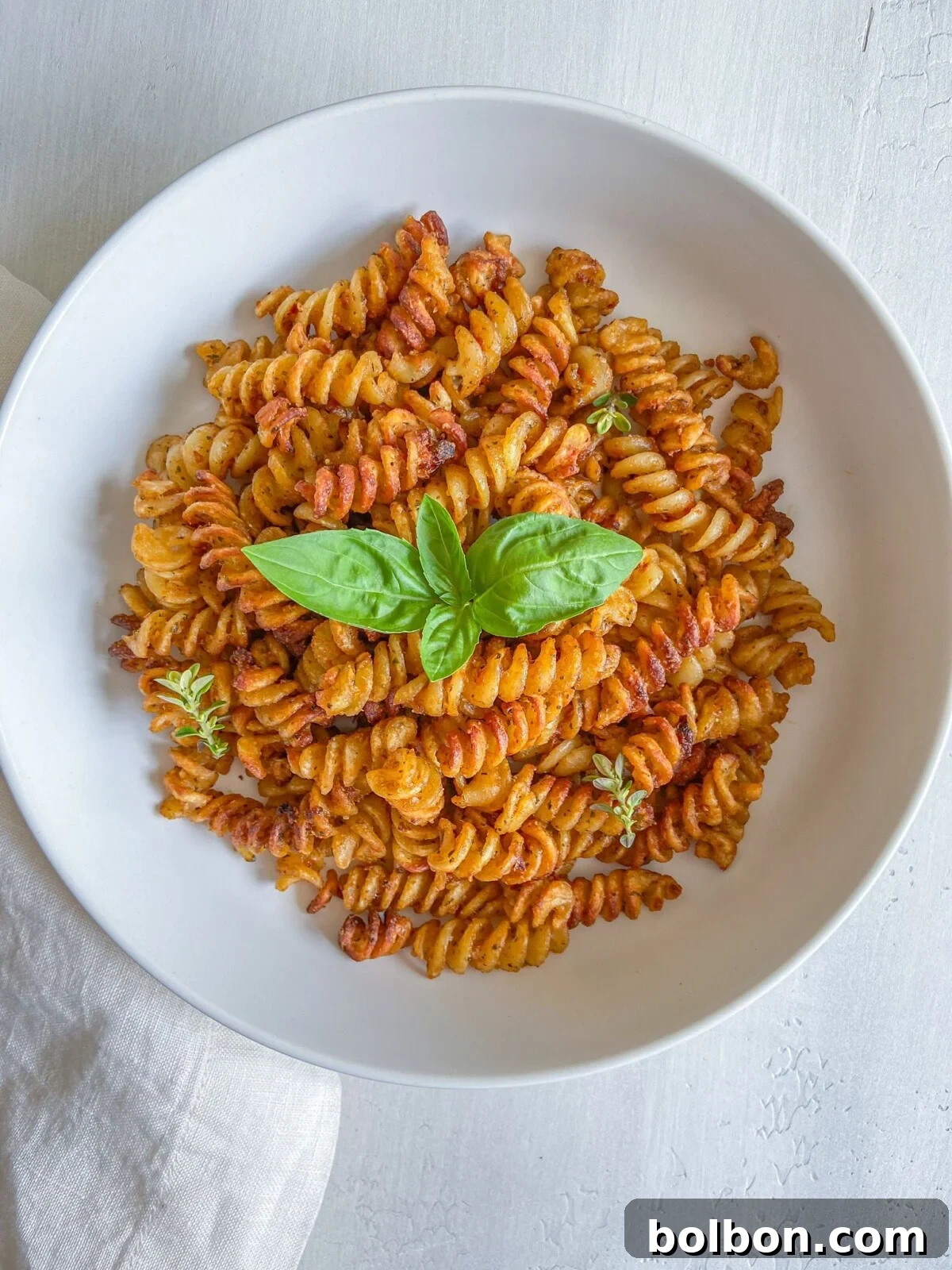 Crispy Pasta Bites 2 Golden rotini pasta chips tossed with basil pesto in a white bowl.