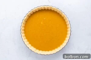 An unbaked pumpkin pie, perfectly filled and ready for the oven, resting in its crimped crust.