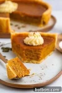 A slice of pumpkin pie on a plate, adorned with a swirl of whipped cream, cinnamon, and a few whole cinnamon sticks.