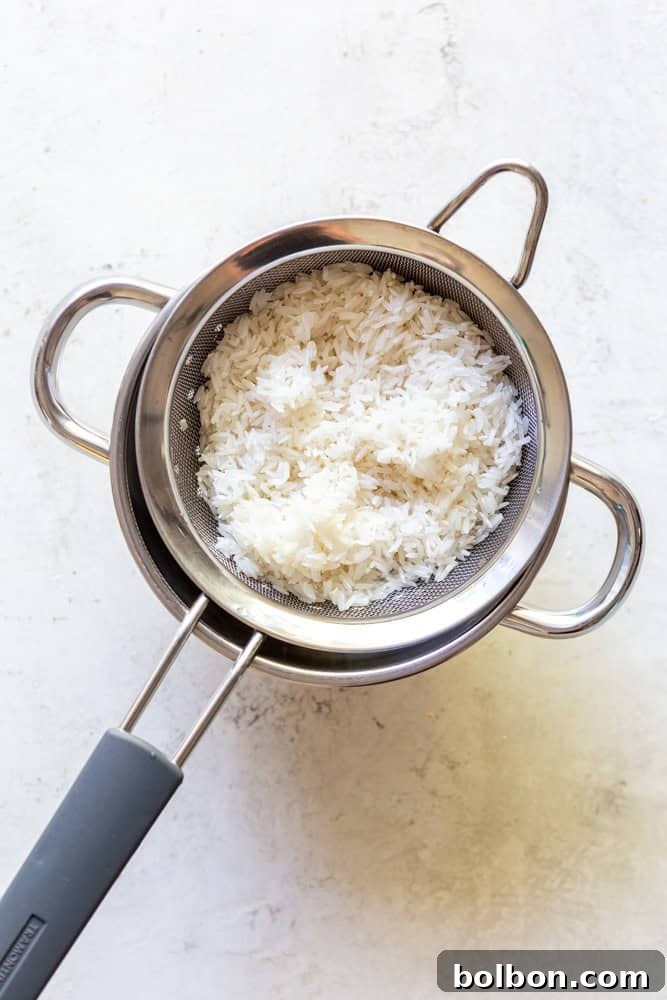 Master the Art of Fluffy White Rice 4 Long grain white rice being rinsed in a stainless steel mesh strainer under running water.