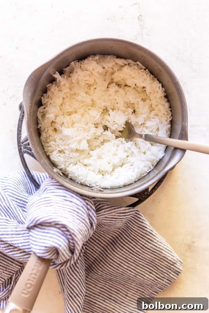 Master the Art of Fluffy White Rice 5 Freshly cooked, fluffy white rice in a saucepan, being fluffed with a fork, ready to serve.