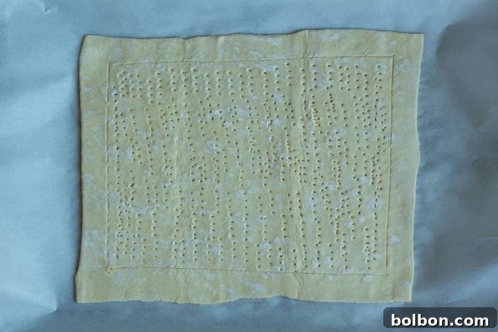 Puff pastry scored and pricked with a fork, ready for the savory filling.