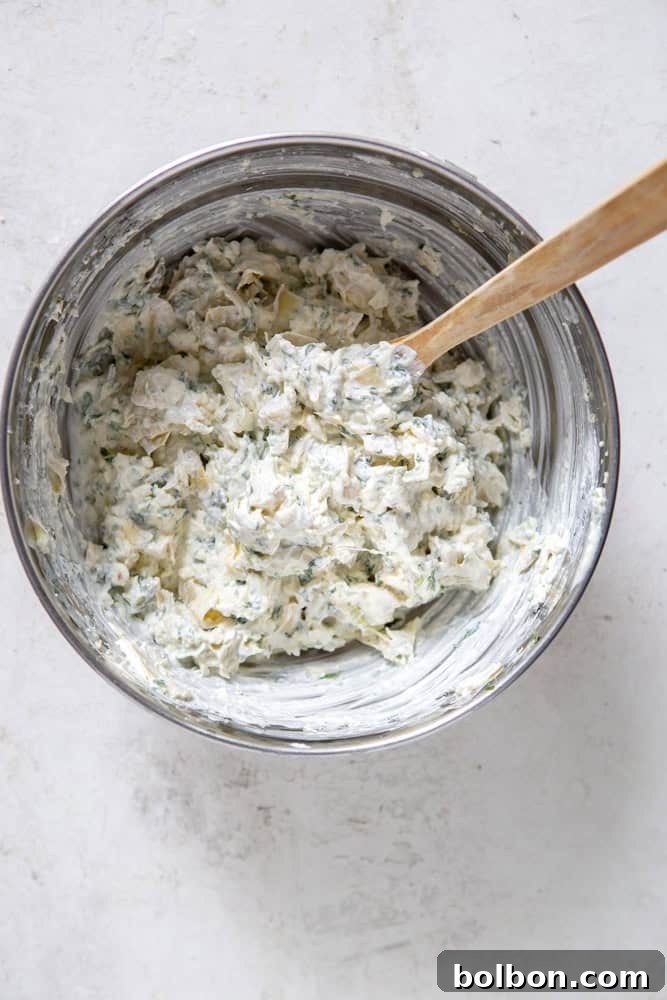 Spinach artichoke dip neatly spread in a white baking dish, ready to be put in the oven.