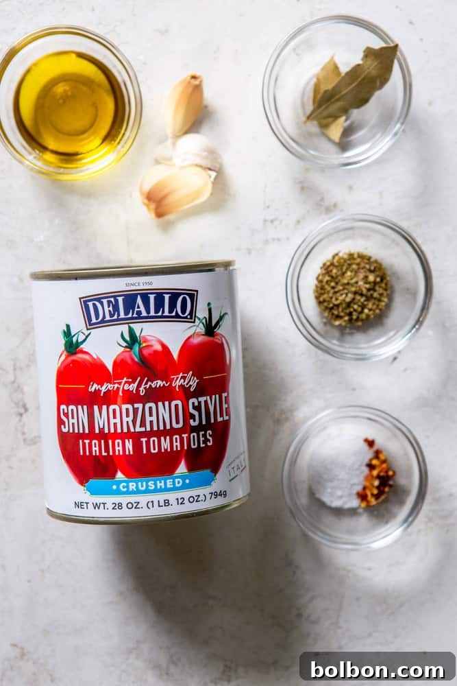Ingredients for Easy Marinara Sauce arranged: a can of crushed tomatoes, olive oil, garlic cloves, bay leaves, dried oregano, salt, pepper, and red pepper flakes.