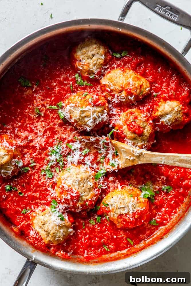Baked Turkey Ricotta Meatballs generously coated in rich red marinara sauce, garnished with fresh herbs and parmesan, presented in a bowl.