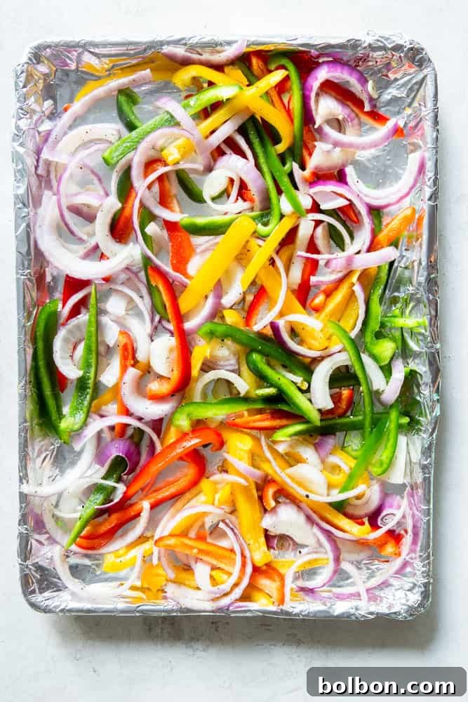 Sheet Pan Steak Fajita Feast 6 Freshly sliced red onions and colorful bell peppers tossed with olive oil and salt, arranged on a sheet pan before cooking.