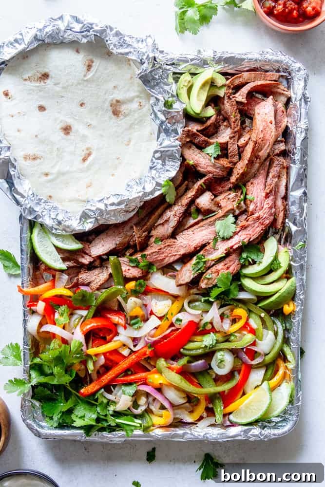 Sheet Pan Steak Fajita Feast 8 Perfectly cooked and sliced flank steak tossed with roasted bell peppers and onions, presented on a sheet pan alongside warm, foil-wrapped tortillas.