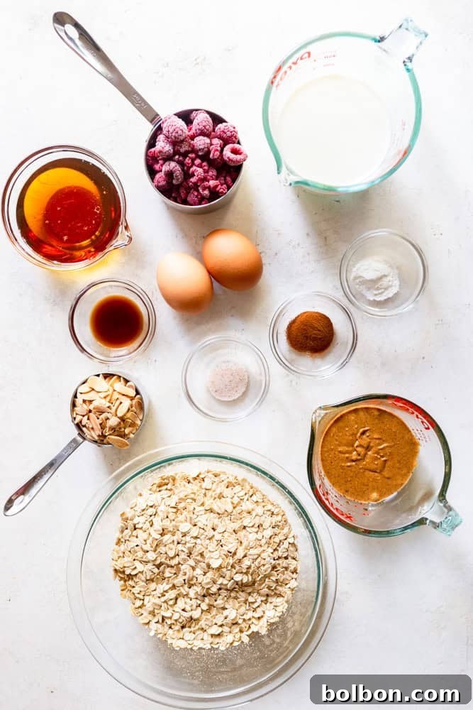 Fresh ingredients for making Raspberry Almond Baked Oatmeal: Rolled oats, sliced almonds, cinnamon, baking powder, sea salt, creamy almond butter, eggs, milk, pure maple syrup, vanilla extract, and fresh raspberries.