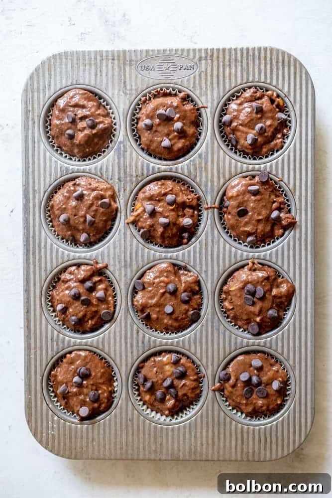 Muffin tin filled with rich chocolate zucchini muffin batter, each cavity perfectly topped and ready for baking to achieve ideal domed tops.