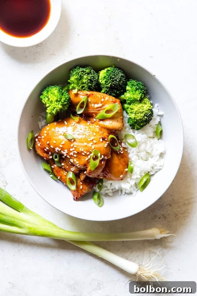 Close-up of golden brown Baked Soy Ginger Chicken Thighs with broccoli and rice in a white bowl, garnished with sesame seeds.