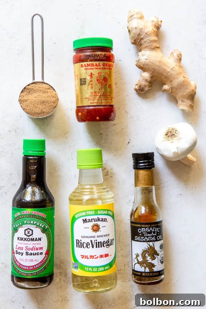 Individual ingredients for soy ginger marinade including low sodium soy sauce, rice vinegar, toasted sesame oil, brown sugar, Sambal Oelek, fresh ginger root and garlic cloves laid out.