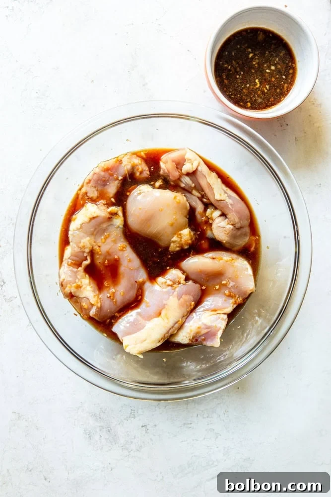 Raw chicken thighs soaking in a soy ginger marinade in a shallow white dish.
