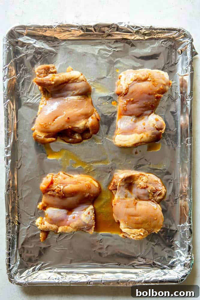 Raw soy ginger chicken thighs arranged on a sheet pan lined with aluminum foil, ready for baking.