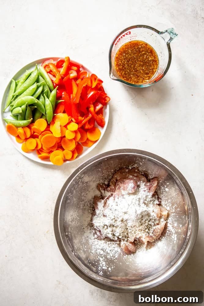Ingredients for Honey Garlic Chicken Stir fry before cooking - honey garlic stir fry sauce, carrots, snap peas, red bell peppers, chicken thighs cut into 1 inch pieces with cornstarch, salt and pepper in a bowl. 