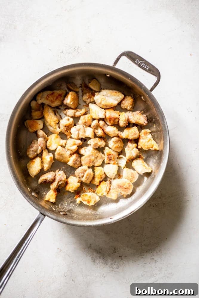 Chicken thigh pieces being cooked in a pan.