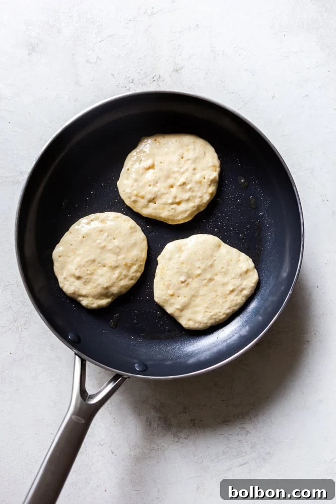 Velvet Banana Pancakes 11 Several banana pancakes cooking evenly on a hot skillet, showing the beginning stages of bubbling and setting.