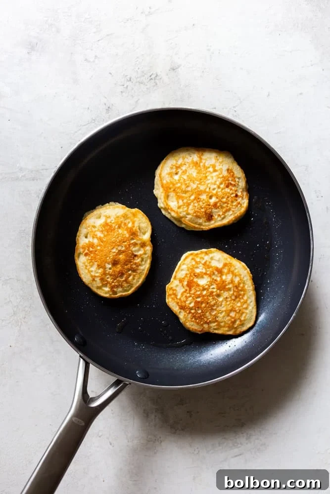 Velvet Banana Pancakes 12 A pancake being flipped on a nonstick pan, showing a golden-brown underside and bubbles forming on the raw side, indicating it's ready.