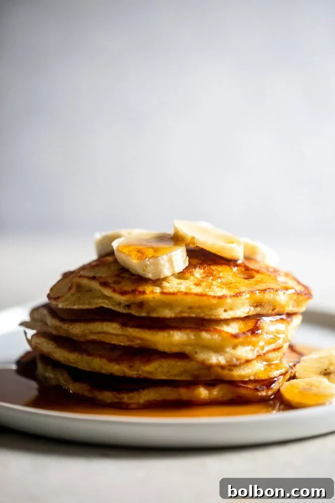 Velvet Banana Pancakes 13 A stack of golden-brown fluffy banana pancakes, garnished with fresh banana slices and a light dusting of powdered sugar, ready to be served.