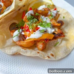 A soft tortilla filled with seasoned grilled chicken, sliced bell peppers, fresh herbs, and drizzled with white sauce—these Easy Chicken Fajitas are served on a white plate with a lemon wedge.