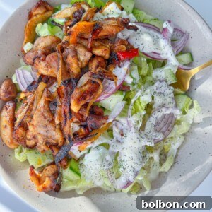 A bowl of Chicken Fajita Salad topped with grilled chicken, sliced red onions, lettuce, cucumber, and drizzled with a creamy dressing, served with a gold fork.