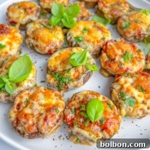 A white plate filled with baked stuffed mushrooms topped with melted cheese, chopped herbs, and garnished with fresh basil leaves.