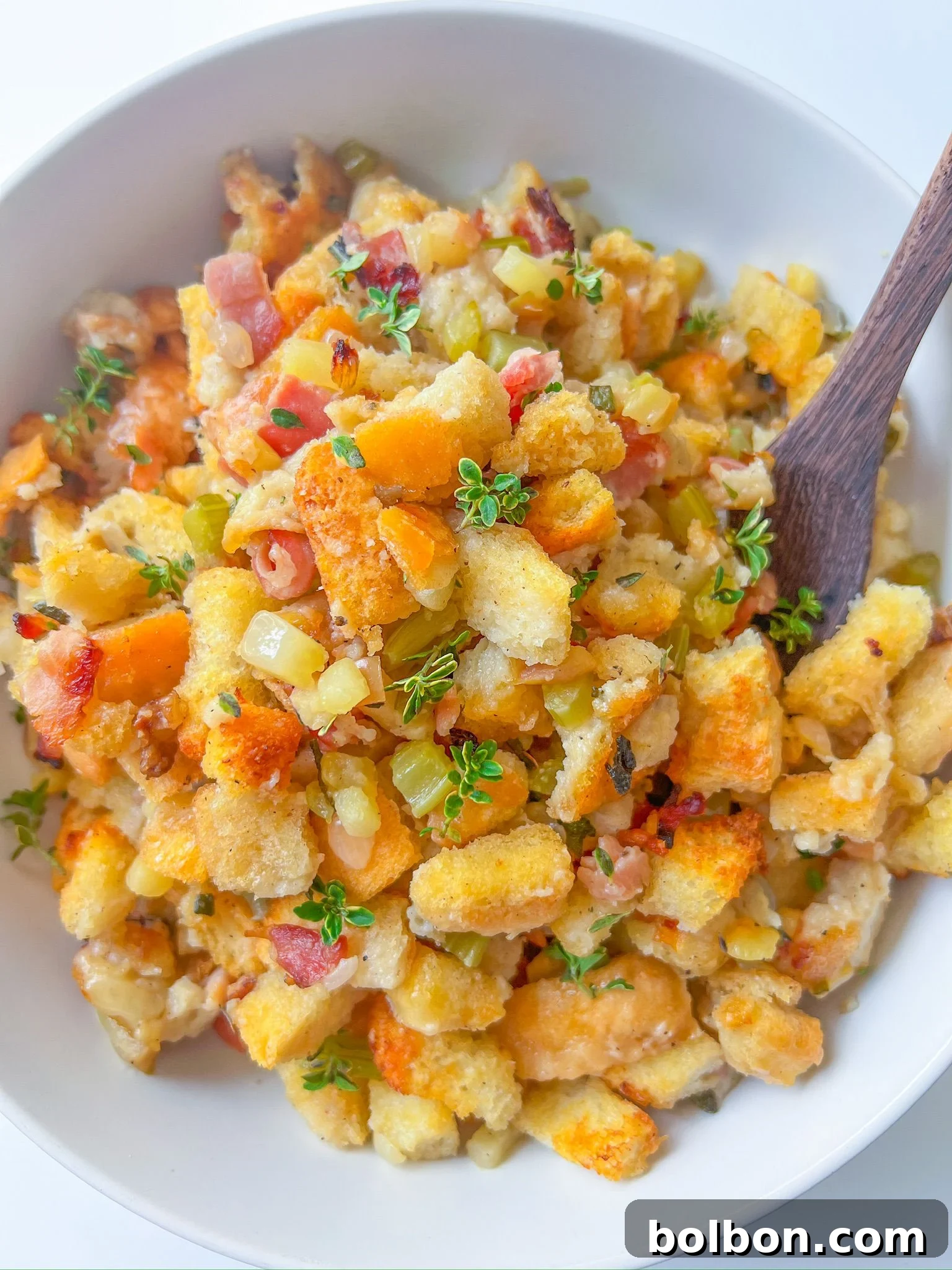 A beautiful bowl of golden-brown Thanksgiving bread stuffing, garnished with fresh thyme, and a wooden spoon resting inside, ready to be served.