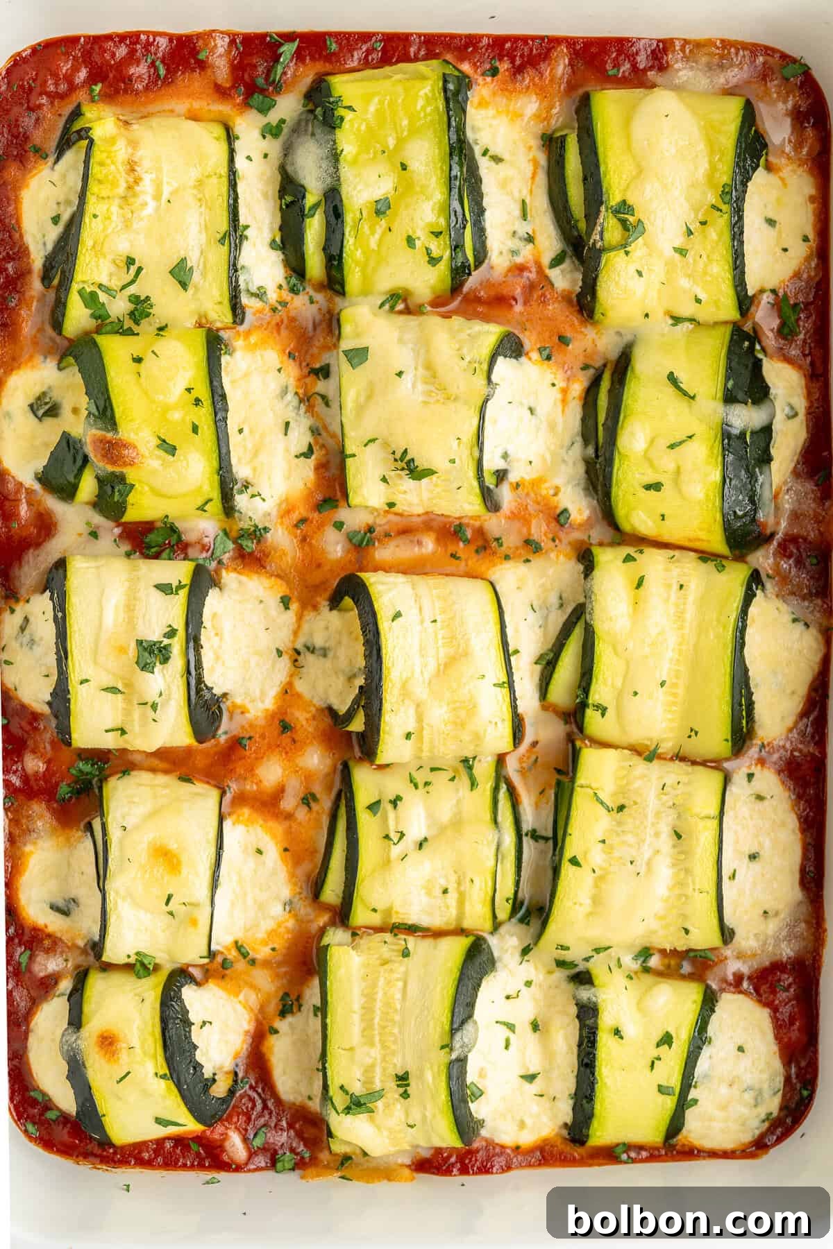 A tray showcasing zucchini rolls filled with ricotta, bathed in marinara sauce and topped with melted cheese.