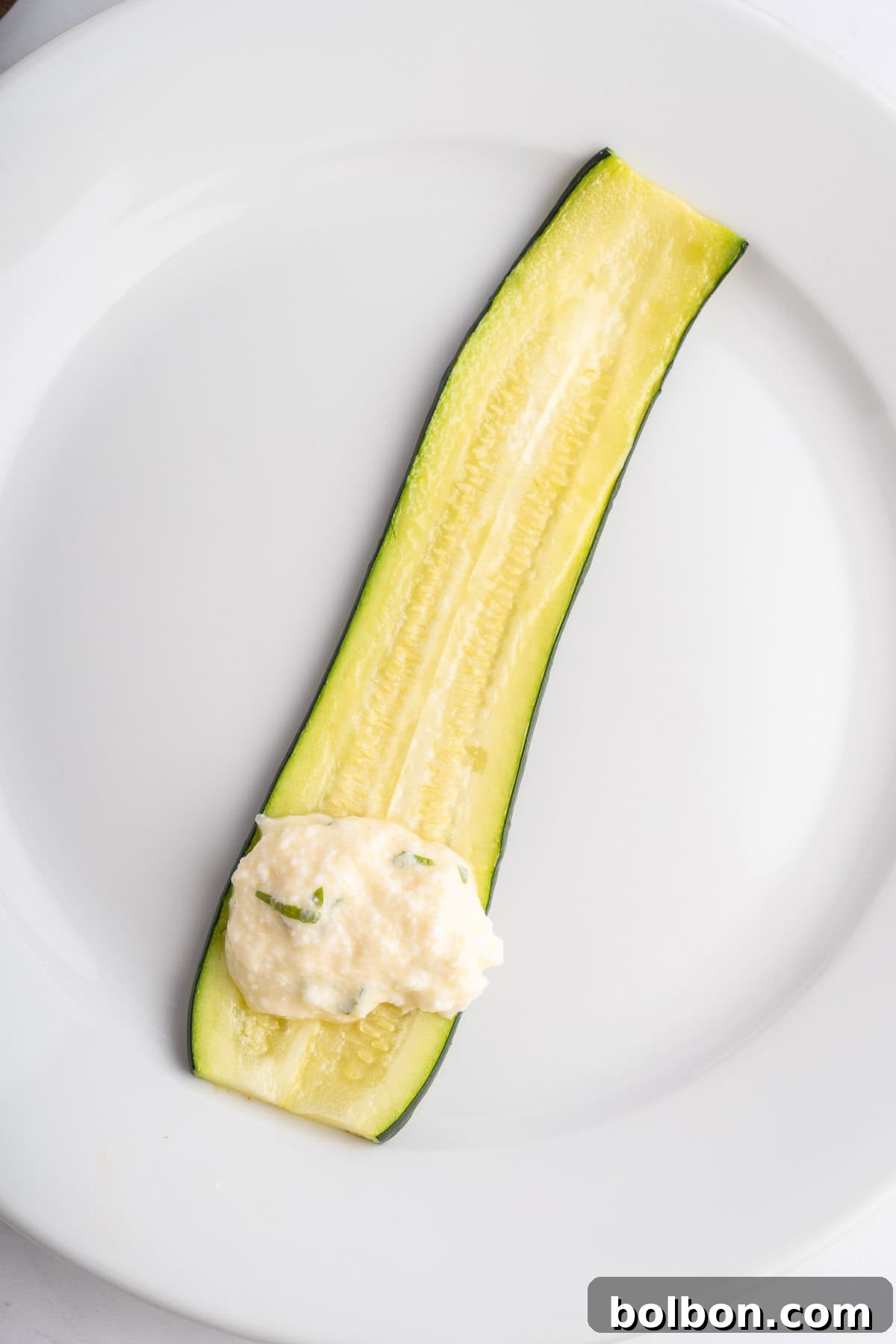 One slice of zucchini on a plate with the filling on one end